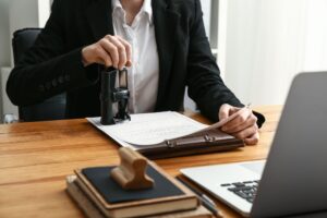 Notary in formal attire stamping a legal document at a desk with office supplies and a laptop, representing certified notary public services.