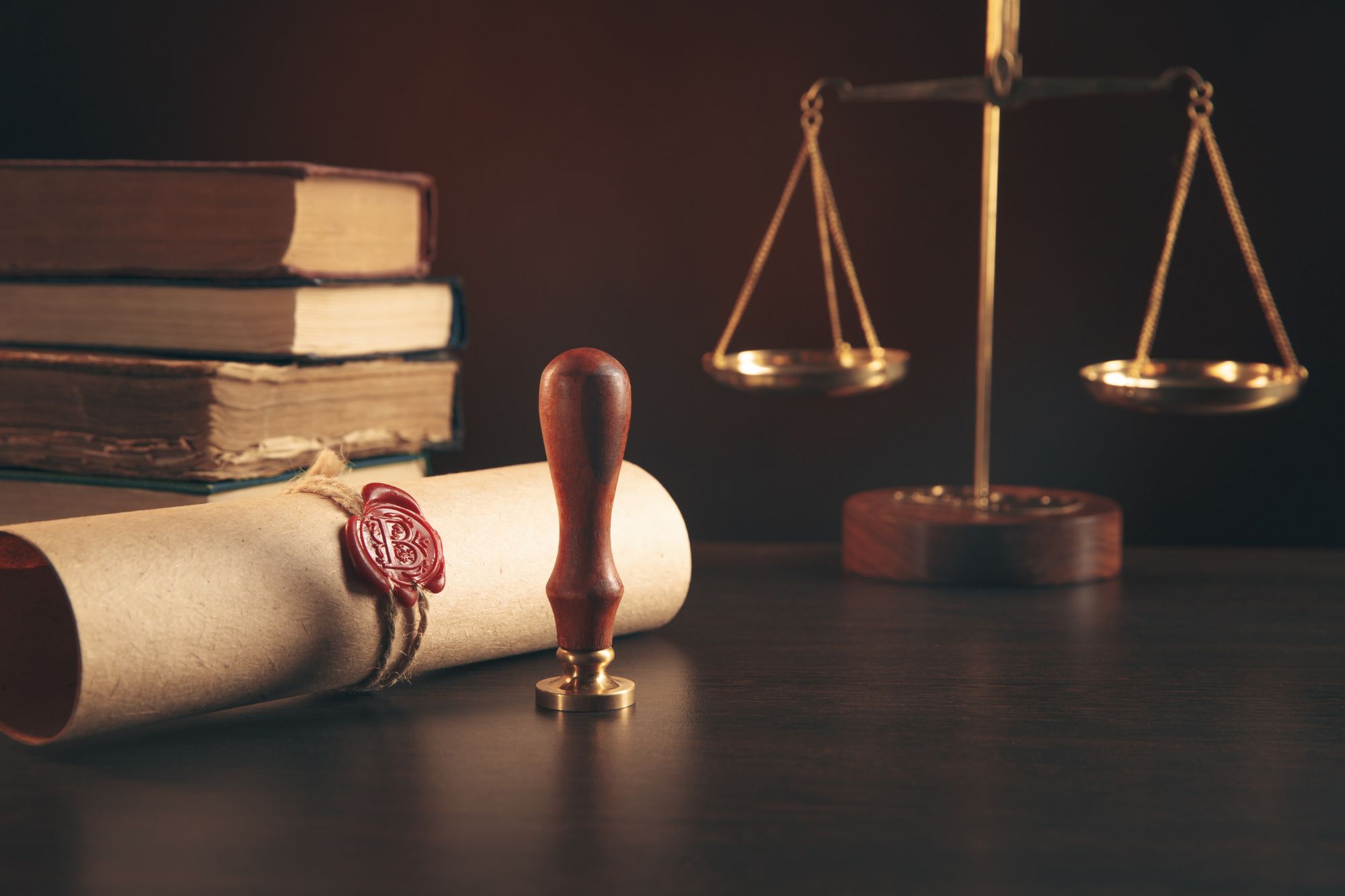 Sealed parchment scroll with wax stamp, wooden seal stamp, and justice scale on a dark desk, symbolizing traditional notarization and legal authority.