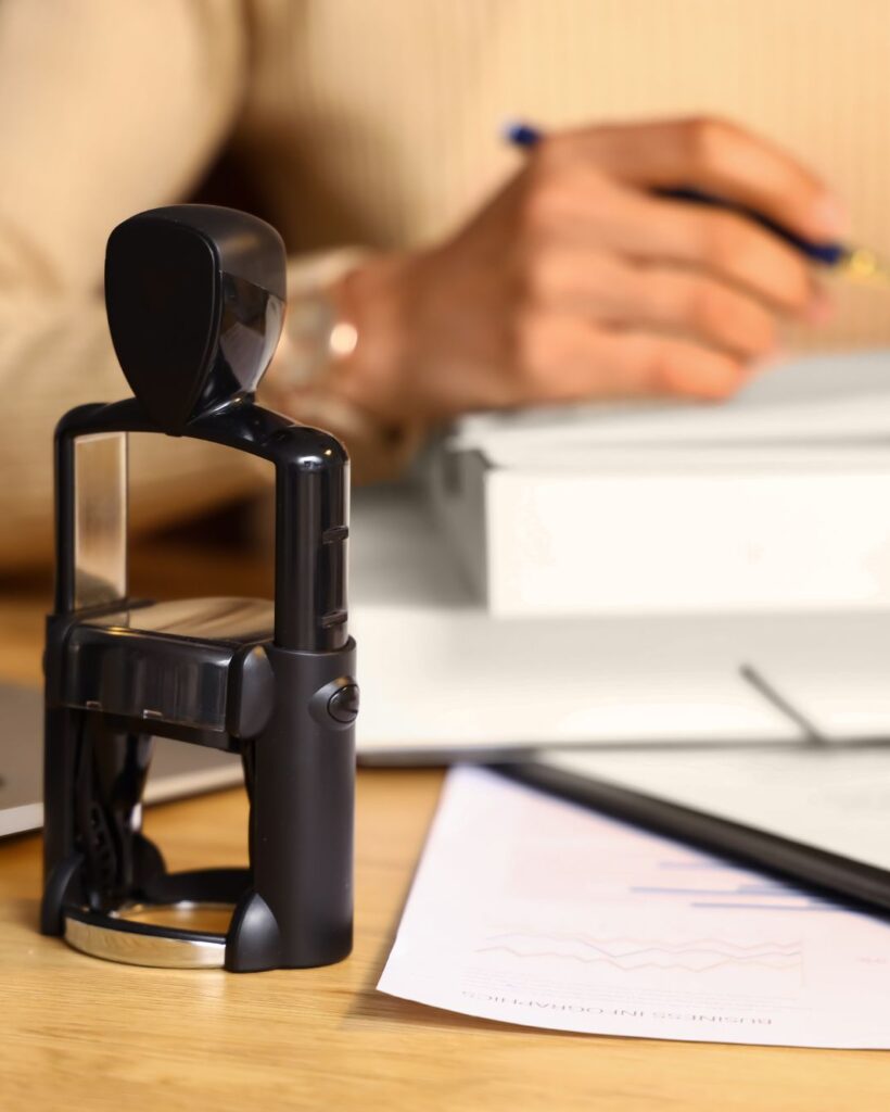 Modern self-inking notary stamp on a desk with business documents and a professional preparing paperwork in the background.