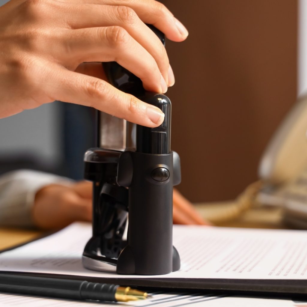 A notary public applying an official stamp to a legal document, completing the notarization process with a seal of approval.